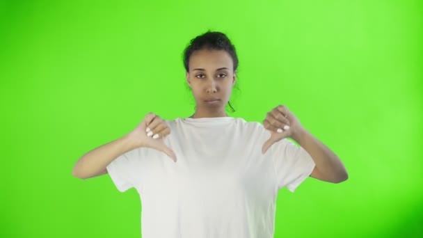Menina bonita em uma camiseta branca mostra polegar para baixo com ambas as mãos no fundo da chave chroma — Vídeo de Stock