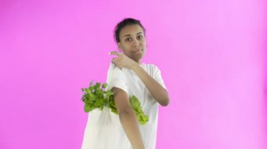 Pembe arka planda sebzeli çanta taşıyan kadın.