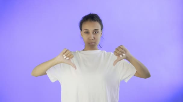 Menina bonita em uma camiseta branca mostra polegar para baixo com as duas mãos no fundo Violet — Vídeo de Stock