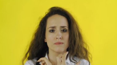 Üzücü, düşünceli, tişörtlü güzel bir kadın. Stüdyoda sarı arka planda duruyor..