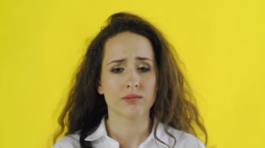 Üzücü, düşünceli, tişörtlü güzel bir kadın. Stüdyoda sarı arka planda duruyor..