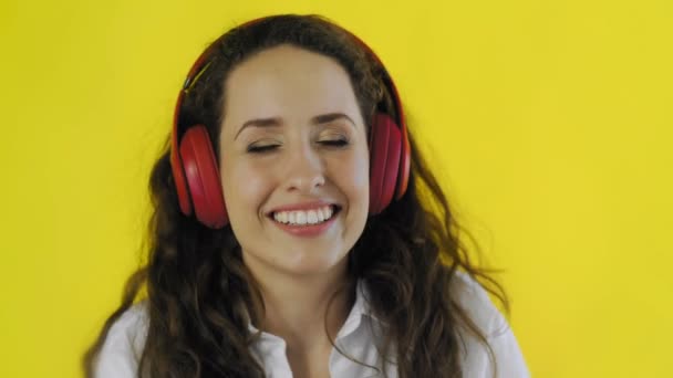 若い魅力的な女性は黄色の背景を持つスタジオでヘッドフォンや笑顔で音楽を聴く. — ストック動画