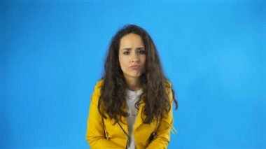 Üzgün, düşünceli, genç, güzel bir kadın. Stüdyoda mavi arka planla omuz silkiyor..