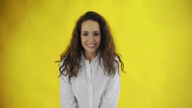 Güzel bir kadın göz kırpıyor ve sarı arka planla stüdyoda ağzını açıyor..