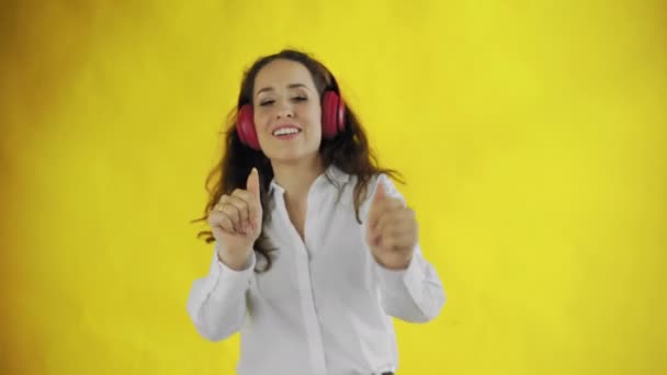 Junge attraktive Frau hört Musik mit Kopfhörern und lächelt im Studio mit gelbem Hintergrund. — Stockvideo
