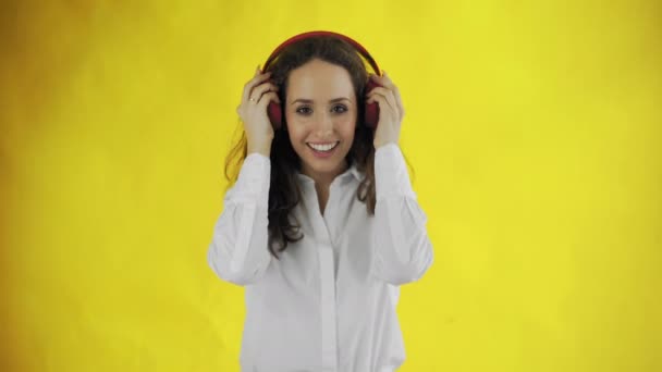 Kvinne som hører på musikk med røde hodetelefoner i Studio med gul bakgrunn. – stockvideo