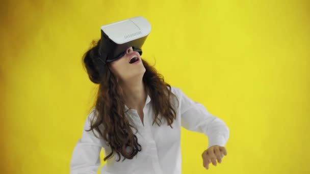 Mujer joven feliz con auriculares de realidad virtual o gafas 3D sobre fondo amarillo en el estudio . — Vídeo de stock