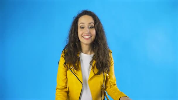 Mladá radostná žena baví smát se zakrývající ústa s rukama v ateliéru s modrým pozadím. — Stock video
