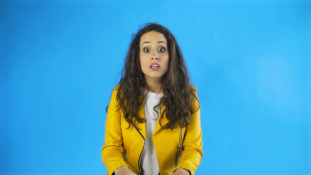 Portret van een verraste vrouw met krullend haar die onverwachts of schokkend uitte in Studio met blauwe achtergrond. — Stockvideo