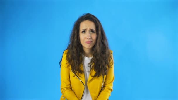 Mujer joven confusa en chaqueta amarilla en Studio con fondo azul . — Vídeos de Stock