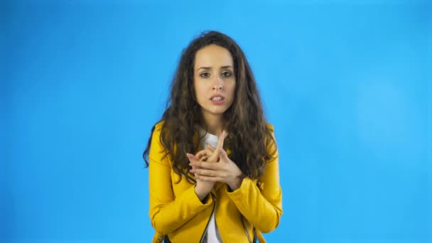 Nerviosa hermosa mujer caucásica con el pelo largo marrón frotando las manos roer las uñas en el estudio con fondo azul . — Vídeos de Stock