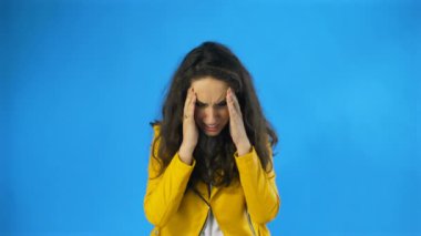 Güzel kız migrenden muzdarip. Mavi arka planda duruyor, ağır çekimde.