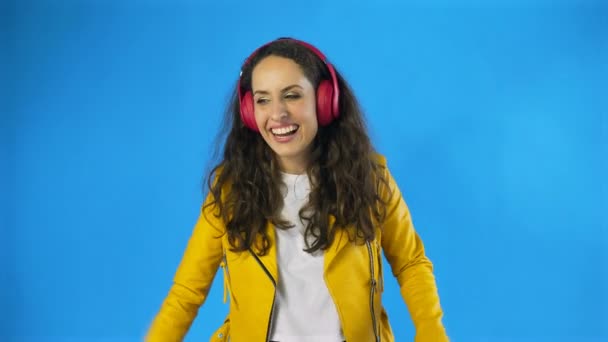 Woman listening to music with red headphones in Studio with blue Background. — Stock Video