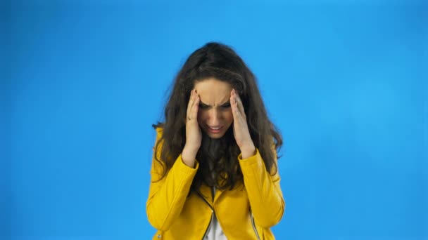 Mooi meisje lijdt aan een migraine staan op een blauwe achtergrond, slow motion — Stockvideo