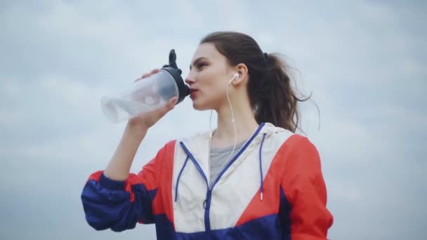 ランニングエクササイズ後にボトルから水を飲むフィットネス女性。フィットネスボトルから飲んで、公園でジョギングするスポーツウーマンの肖像. — ストック動画