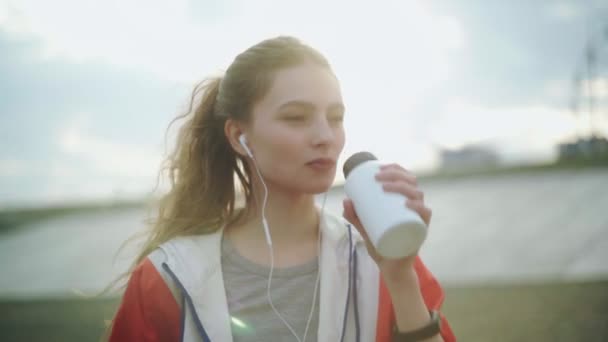 Morena adolescente bebiendo agua fría después de correr en el parque. Hermosa mujer atleta de fitness beber agua después del ejercicio, la salud y el deporte, la luz de la bengala — Vídeos de Stock