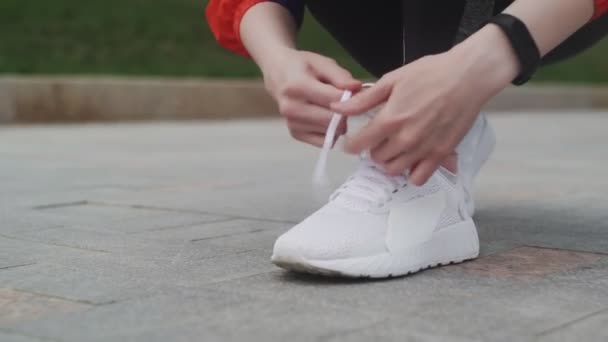 Atleta mujer ata cordones, zapatillas blancas, calcetines blancos, en ropa deportiva, corre por la calle . — Vídeo de stock