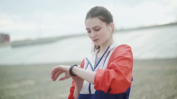 Chica corriendo con un reloj inteligente. Mujer en auriculares con reloj inteligente sobre fondo marino . — Vídeos de Stock