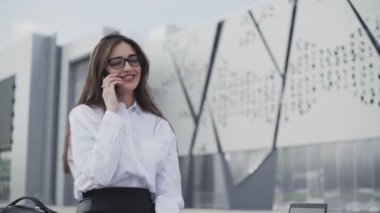 Akıllı telefondan konuşan şık bir kadın. Ofisinin yanındaki bankta oturuyor.