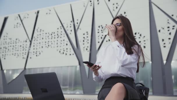 Mulher de negócios bonita em óculos bebendo café e olhando para seu smartphone — Vídeo de Stock