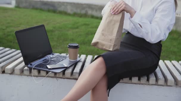 Mujer de negocios irreconocible comiendo un croissant y tomando café en el parque — Vídeo de stock