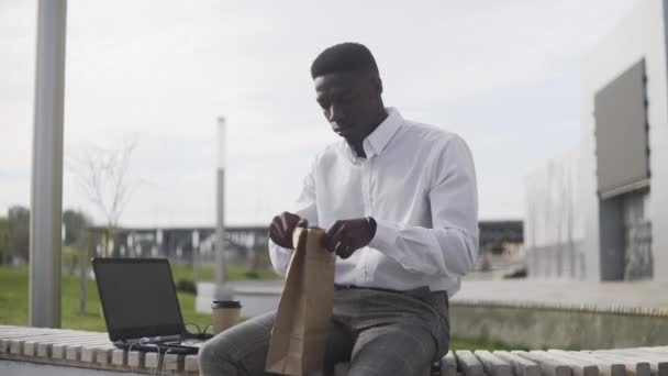 Umtriebiger afrikanischer Geschäftsmann beim Mittagessen und Arbeiten im Freien — Stockvideo