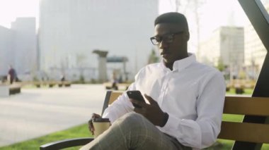Ciddi Afrikalı adam parkta bankta oturuyor ve not defterine notlar yazıyor..