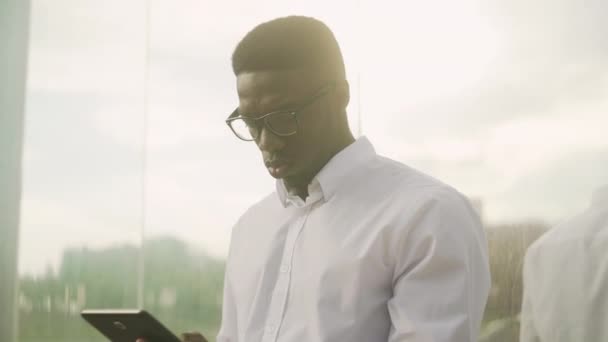Uomo d'affari afroamericano in occhiali che parla al cellulare, in piedi vicino alla parete dello specchio — Video Stock