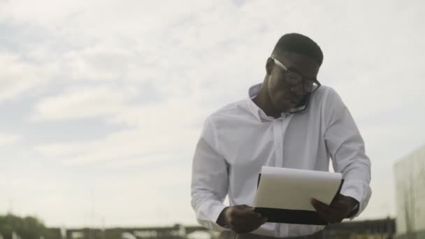 Homme d'affaires afro-américain dans des lunettes marchant dans le bureau et parlant sur un téléphone portable — Video