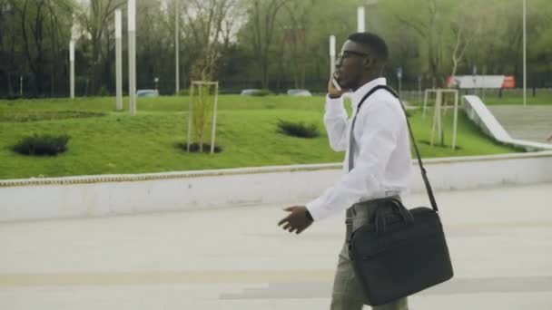 Stylish African American businessman wearing white shirt and grey pants drinking coffee while walking into office — Stock Video