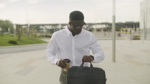 Gros plan de l'homme afro-américain portant une chemise blanche buvant du café et utilisant son téléphone — Video