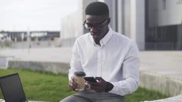 Homme d'affaires afro-américain élégant enregistrant un message vocal tout en étant assis dans le parc près du bureau — Video