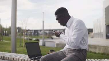 Ofis yakınındaki parkta otururken sesli mesaj kaydeden genç işadamının yan görünümü