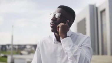 Şehir parkında cep telefonuyla konuşan diş telleri ve gözlükleri olan genç Afrikalı Işadamı