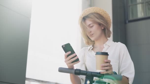 Kadın akıllı telefon kullanıyor ve elektrik motoruna bindikten sonra kahve içiyor. — Stok video