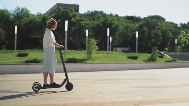 VISTA DE LADO Mulher atraente montando uma cidade elétrica compartilhada scooter no parque da cidade — Vídeo de Stock