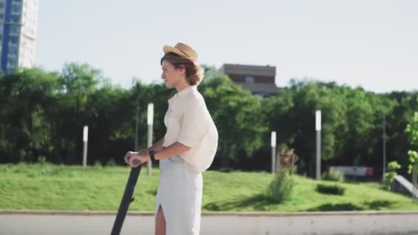 Aantrekkelijke vrouw in stro hoed rit op de elektrische kick scooter — Stockvideo