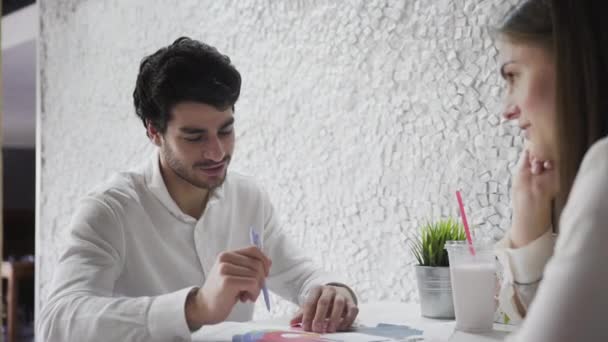 Dos jóvenes empresarios sentados en una mesa mientras discuten los planes de negocios diarios utilizan documentos y gráficos — Vídeo de stock