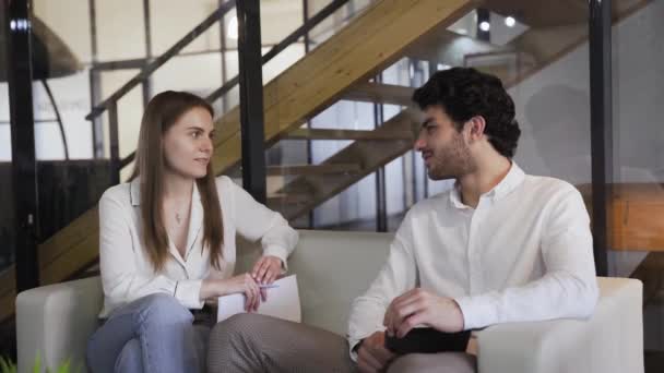 Junges elegant gekleidetes Paar sitzt auf einem weißen Sofa und redet. — Stockvideo