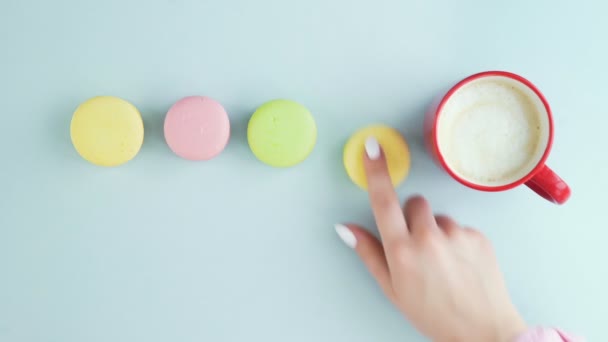 Macarrones o macarones en superficie azul pastel con café en taza roja. — Vídeo de stock