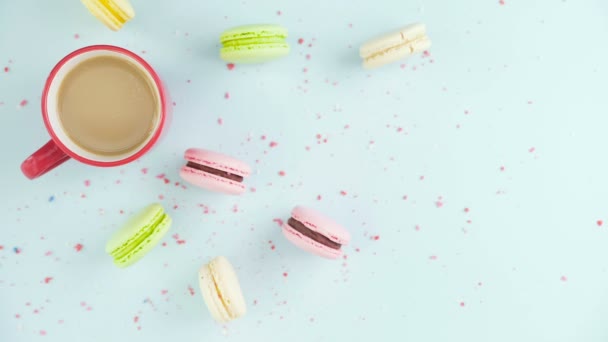 Macarrones o macarones en superficie azul pastel con café en taza roja. — Vídeo de stock