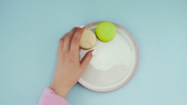 Tatlı renkli badem kurabiyeleri ya da pastel mavi yüzeyde beyaz tabakta makaron..