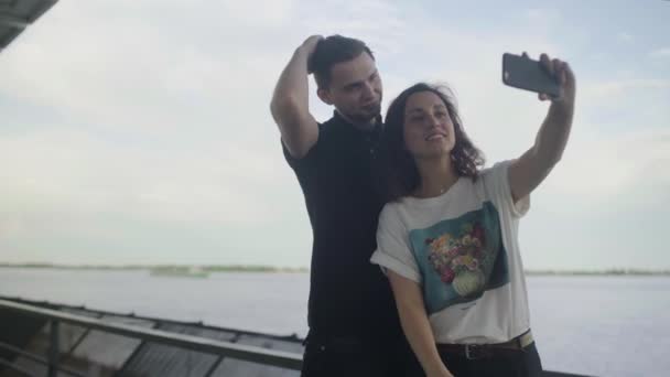 Divertida joven pareja enamorada haciendo fotos cerca del río — Vídeo de stock