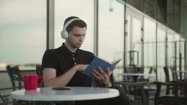 Beau homme écoutant de la musique sur écouteurs et livre de lecture — Video