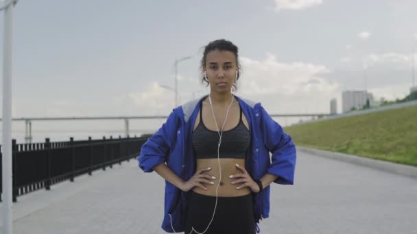 Портрет афроамериканки бігунки з навушниками дивитися на камеру — стокове відео