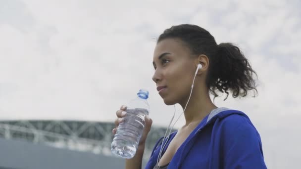 Афро-американская бегунья пьет воду после бега. Портрет Фитнес-женщина пьет воду из бутылки . — стоковое видео