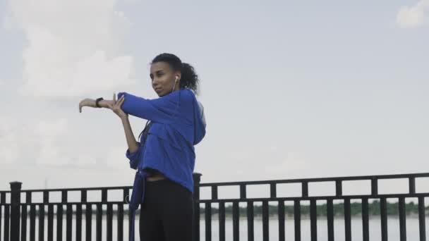 Afroamerikanische Läuferin streckt ihre Arme aus, um auf der Straße zu laufen, Gesunde junge schöne Frau bewegt sich in der Nähe des Flusses. — Stockvideo
