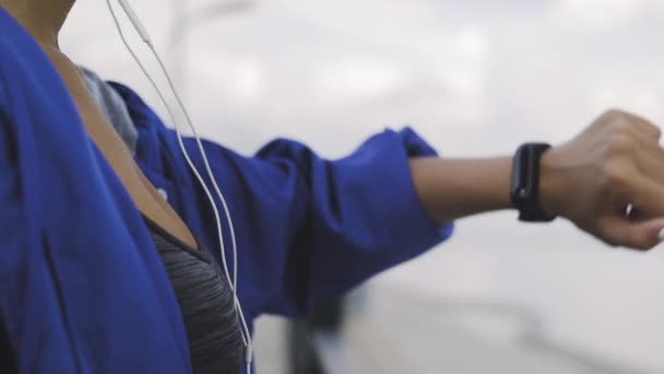 Αφρο-αμερικανική δρομέας γυναίκα με ακουστικά χρησιμοποιώντας βραχιόλι γυμναστικής πριν από την εκτέλεση — Αρχείο Βίντεο