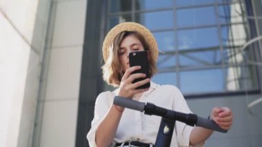 Kadın elektrikli scooter 'a bindikten sonra akıllı telefon kullanıyor.