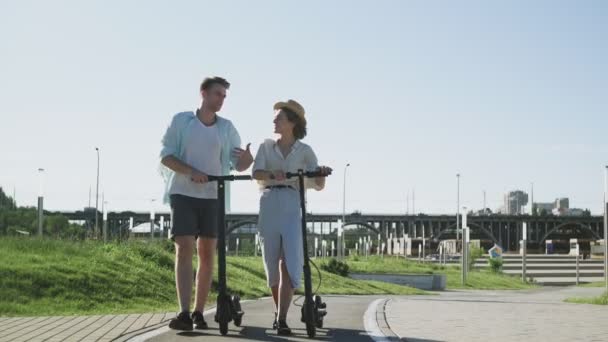 Happy Couple Walk con sus scooters eléctricos en el parque de verano — Vídeos de Stock